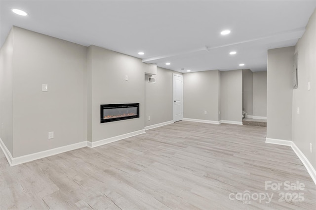 basement featuring recessed lighting, baseboards, a glass covered fireplace, and light wood-type flooring