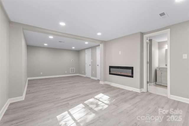 unfurnished living room featuring visible vents, recessed lighting, light wood-style floors, and a glass covered fireplace