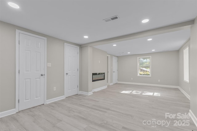 unfurnished living room featuring a glass covered fireplace, recessed lighting, light wood-style flooring, and visible vents
