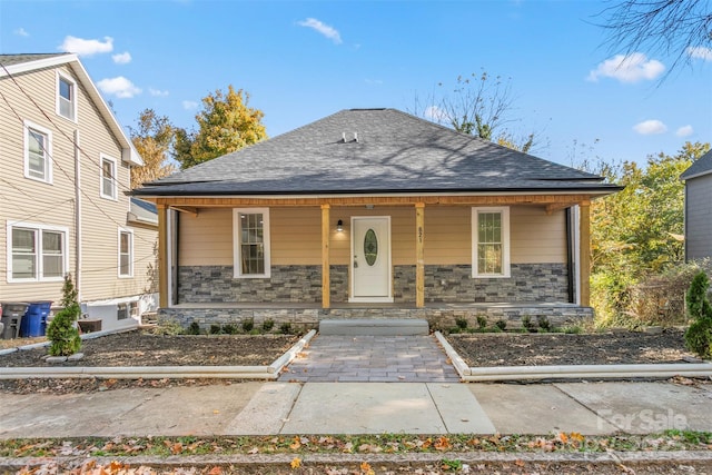 bungalow-style house featuring roof with shingles, a porch, and stone siding