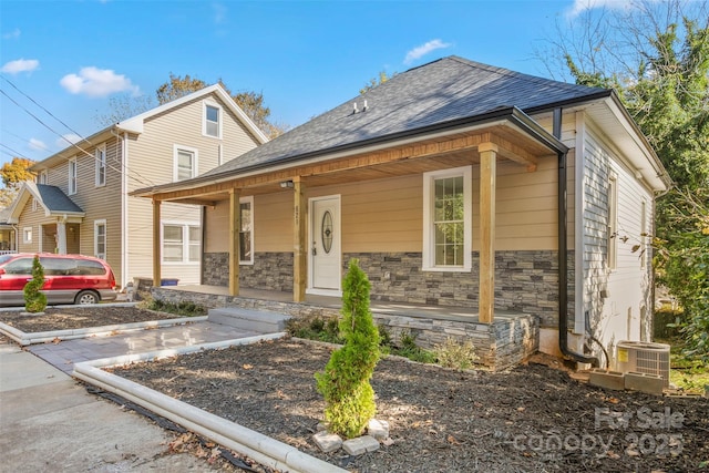 view of front of home featuring central AC unit, a shingled roof, a porch, and stone siding