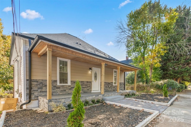 view of front of house featuring a porch, a shingled roof, and stone siding