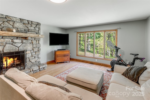 living area with baseboards, a stone fireplace, and wood finished floors