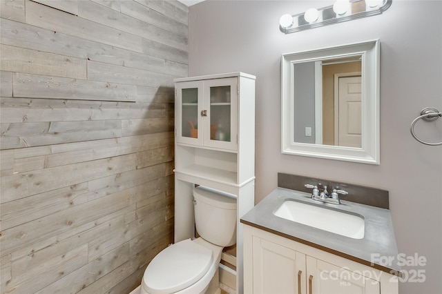 bathroom with toilet, wood walls, and vanity