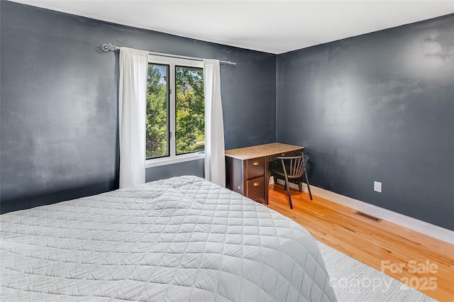 bedroom with baseboards, visible vents, and wood finished floors