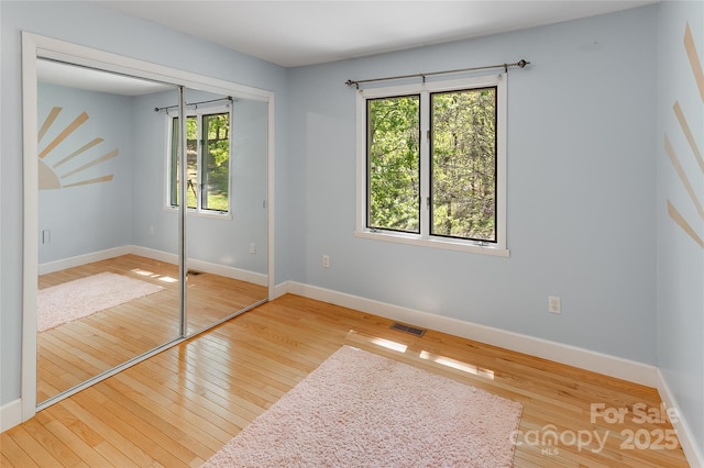 unfurnished bedroom featuring multiple windows, a closet, and hardwood / wood-style floors