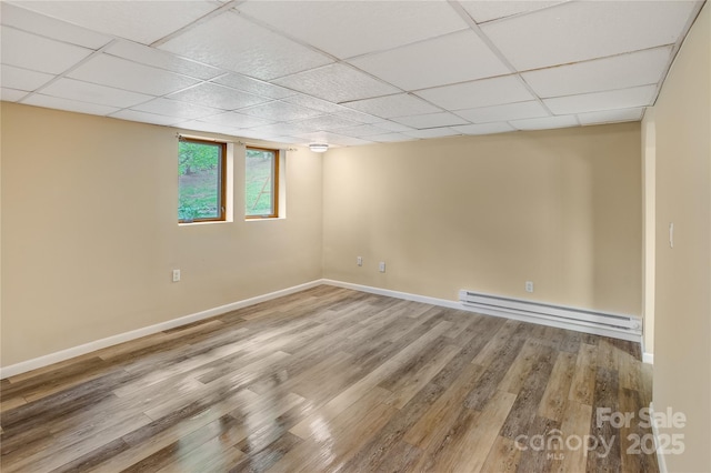 below grade area with baseboards, a drop ceiling, wood finished floors, and baseboard heating