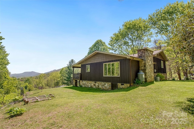 view of property exterior with stone siding, a mountain view, a yard, and a chimney