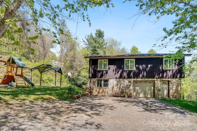 exterior space featuring a garage, a playground, aphalt driveway, a front lawn, and stone siding