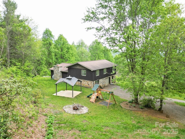 rear view of house with a gazebo, a playground, an outdoor fire pit, a yard, and stone siding