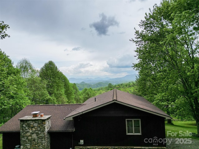 view of side of property featuring a forest view, a mountain view, and roof with shingles