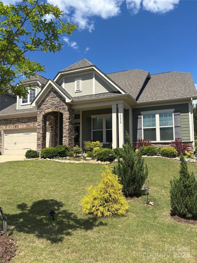 view of front facade with a front lawn, roof with shingles, and stone siding