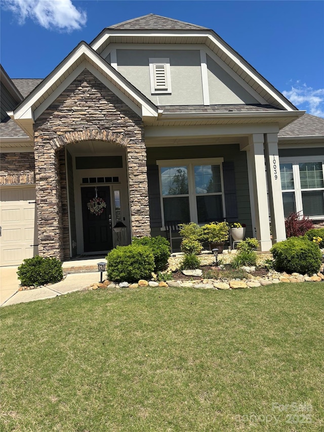 entrance to property featuring stone siding, covered porch, an attached garage, a shingled roof, and a yard