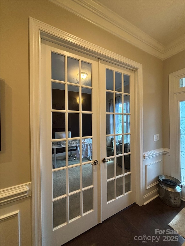 doorway to outside featuring french doors, a wainscoted wall, crown molding, a decorative wall, and dark wood-style flooring