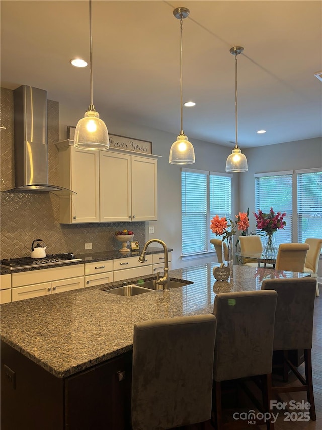 kitchen with a sink, stainless steel gas cooktop, a center island with sink, wall chimney exhaust hood, and decorative backsplash