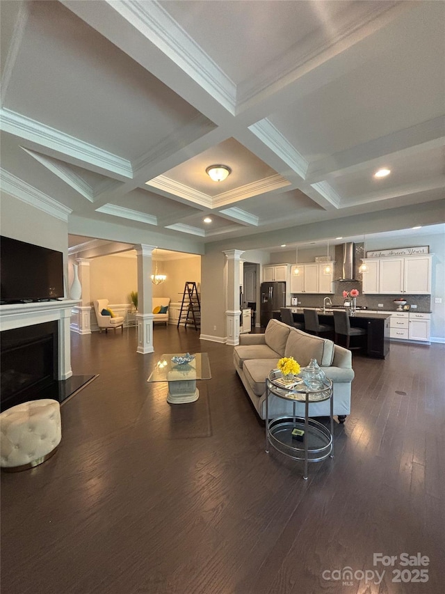 living room featuring ornate columns, coffered ceiling, beam ceiling, dark wood-style flooring, and ornamental molding
