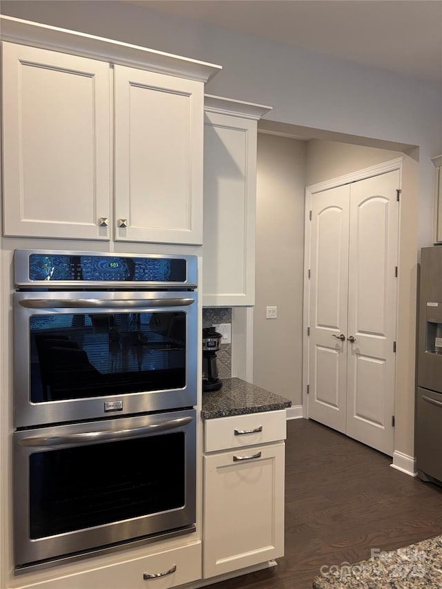 kitchen with stainless steel appliances, dark stone counters, dark wood-style flooring, white cabinets, and baseboards