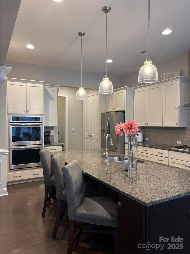 kitchen featuring a sink, tasteful backsplash, dark wood finished floors, white cabinetry, and appliances with stainless steel finishes