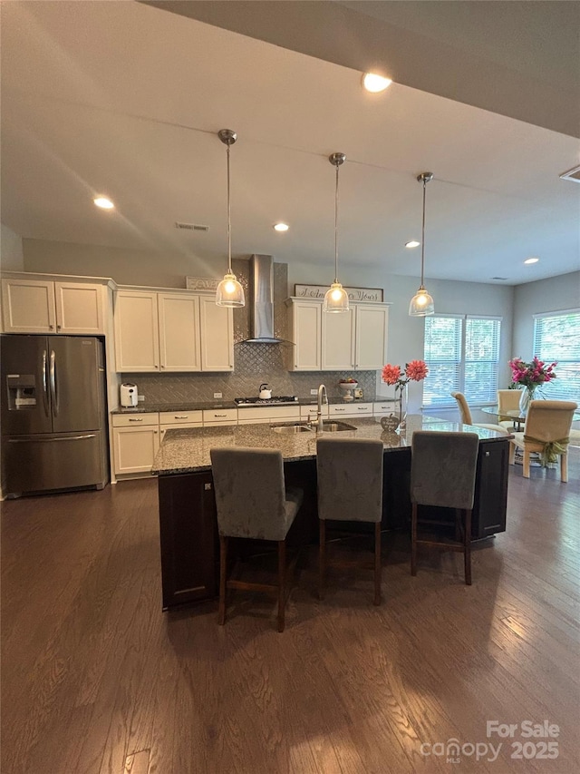 kitchen featuring dark wood finished floors, a sink, wall chimney exhaust hood, stainless steel appliances, and white cabinets