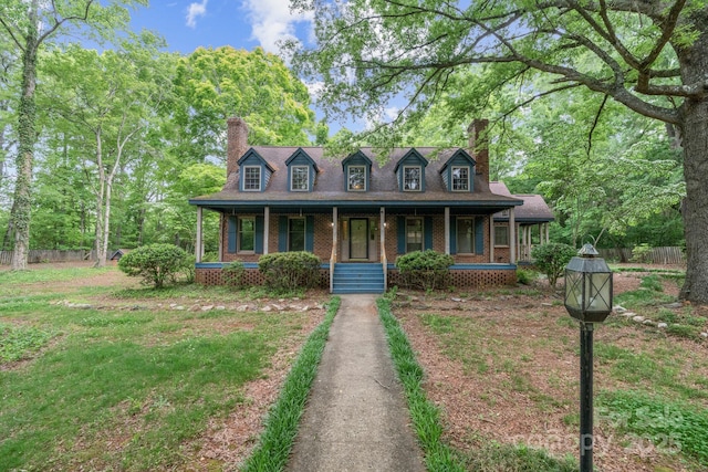 new england style home with a porch, fence, a chimney, and brick siding