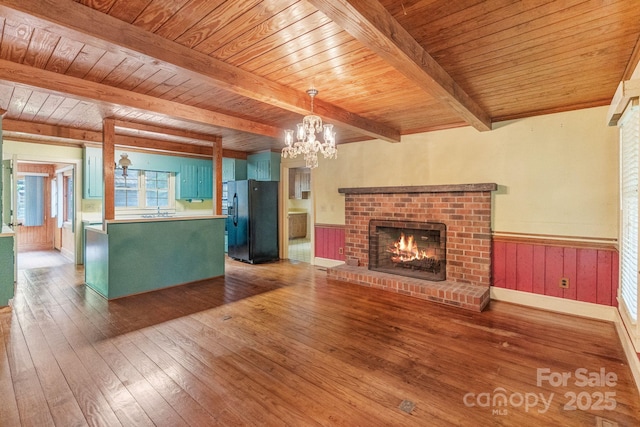 unfurnished living room featuring beam ceiling, wooden ceiling, a fireplace, a chandelier, and wood-type flooring