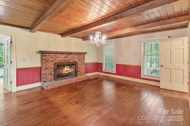 unfurnished living room featuring a wainscoted wall, wooden ceiling, a brick fireplace, and hardwood / wood-style flooring