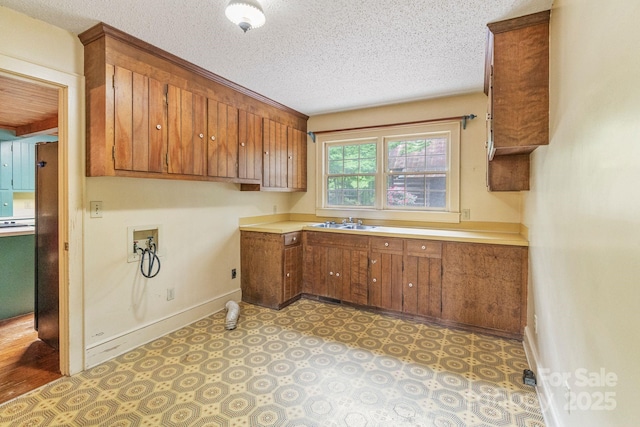 laundry room with a sink, cabinet space, a textured ceiling, baseboards, and hookup for a washing machine