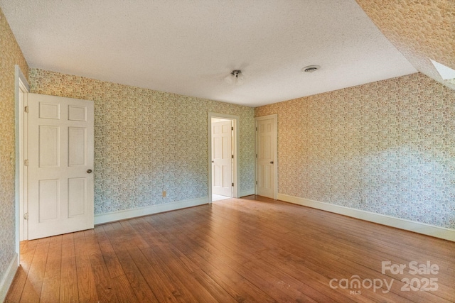 empty room with a textured ceiling, hardwood / wood-style floors, and wallpapered walls