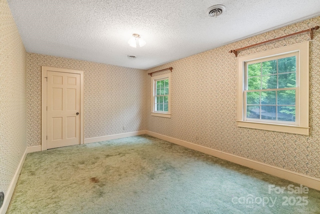 carpeted empty room with wallpapered walls, a healthy amount of sunlight, visible vents, and a textured ceiling