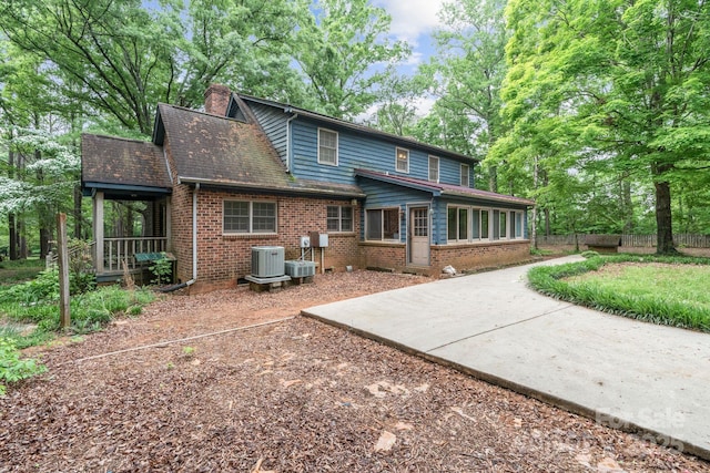 rear view of house featuring fence, a chimney, brick siding, and central AC