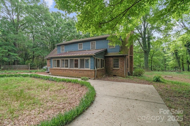 view of front facade with a sunroom, concrete driveway, brick siding, and fence