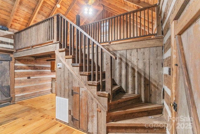 staircase with wood ceiling, lofted ceiling with beams, hardwood / wood-style floors, visible vents, and wooden walls
