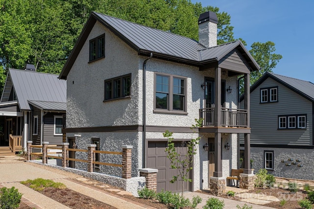 view of front facade featuring an attached garage, stucco siding, a standing seam roof, and a chimney