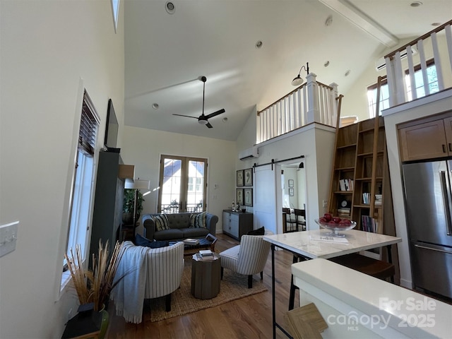living room featuring a barn door, plenty of natural light, ceiling fan, high vaulted ceiling, and wood finished floors