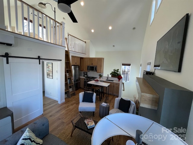 living area with a ceiling fan, a wall unit AC, high vaulted ceiling, light wood-type flooring, and a barn door