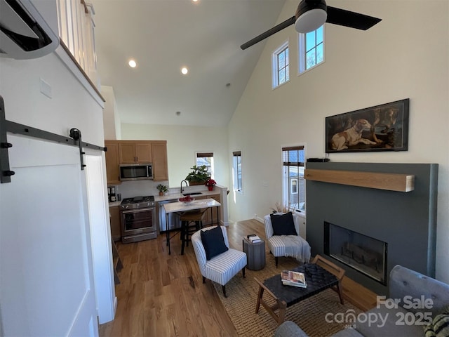living room featuring a healthy amount of sunlight, a barn door, high vaulted ceiling, and a ceiling fan