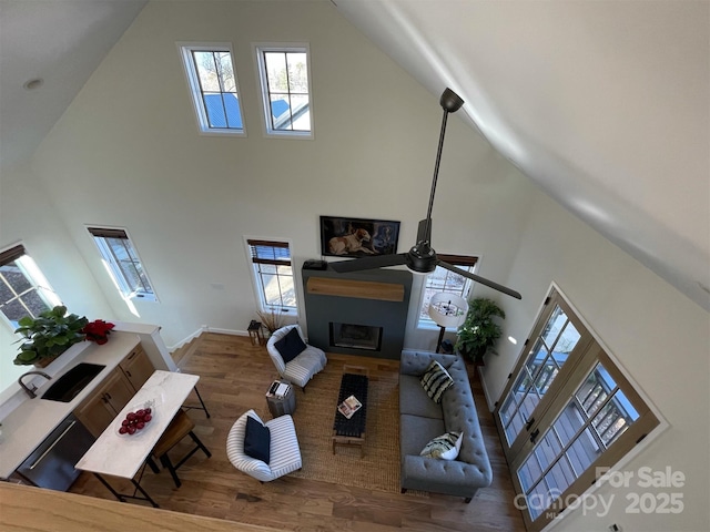 living room with wood finished floors, high vaulted ceiling, a fireplace, a ceiling fan, and baseboards