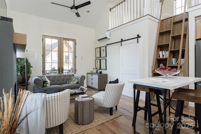 living area with wood finished floors, a ceiling fan, a wall unit AC, high vaulted ceiling, and a barn door