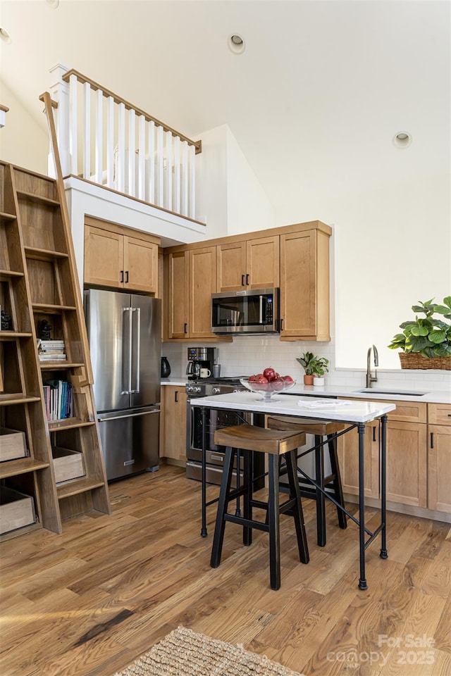 kitchen with a sink, appliances with stainless steel finishes, light countertops, light wood-style floors, and decorative backsplash