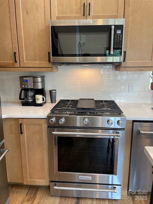 kitchen featuring light countertops, light wood-style flooring, appliances with stainless steel finishes, and tasteful backsplash