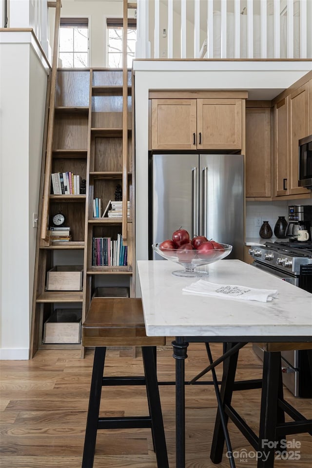 kitchen featuring light wood-type flooring, stainless steel appliances, baseboards, and backsplash