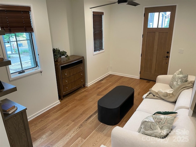 living room featuring light wood finished floors, baseboards, and ceiling fan