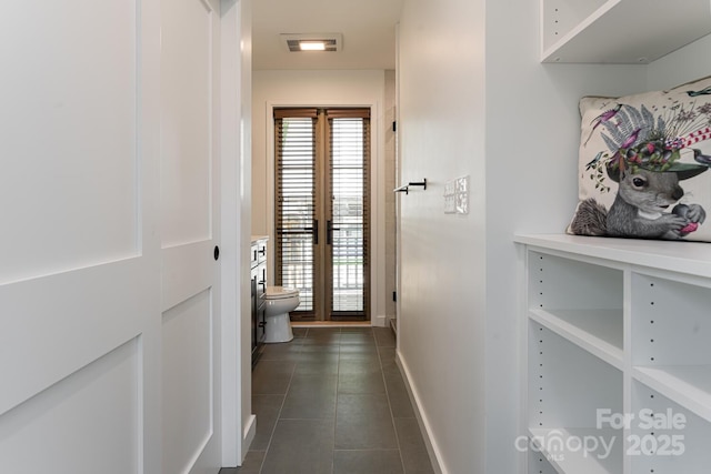 corridor featuring baseboards, a healthy amount of sunlight, visible vents, and dark tile patterned floors