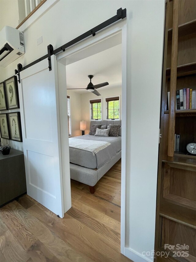 bedroom featuring ceiling fan, wood finished floors, a barn door, and a wall unit AC
