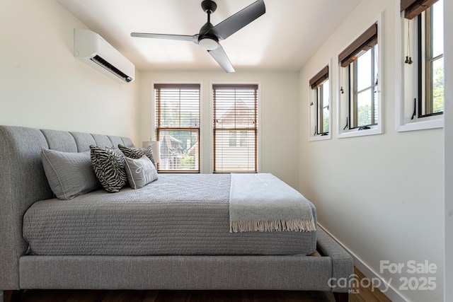 bedroom with an AC wall unit, baseboards, a ceiling fan, and wood finished floors