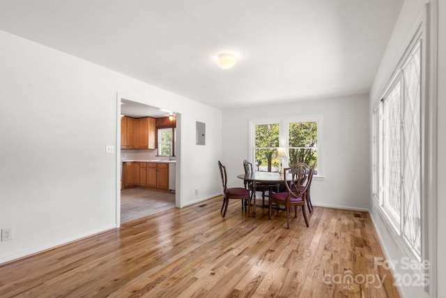 dining space with light wood-style flooring, baseboards, and electric panel
