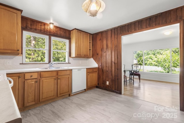 kitchen with dishwasher, a sink, light countertops, tasteful backsplash, and wooden walls