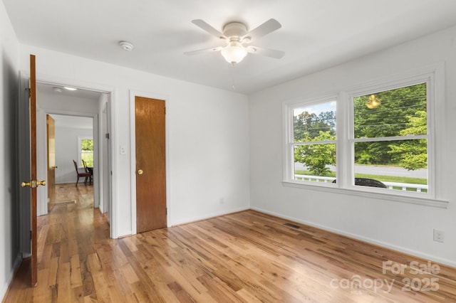 spare room with light wood-type flooring, a ceiling fan, a smoke detector, and baseboards