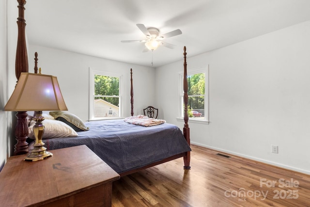 bedroom with multiple windows, wood finished floors, and baseboards