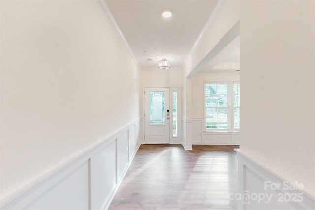 foyer with a decorative wall, crown molding, light wood-style flooring, wainscoting, and a notable chandelier
